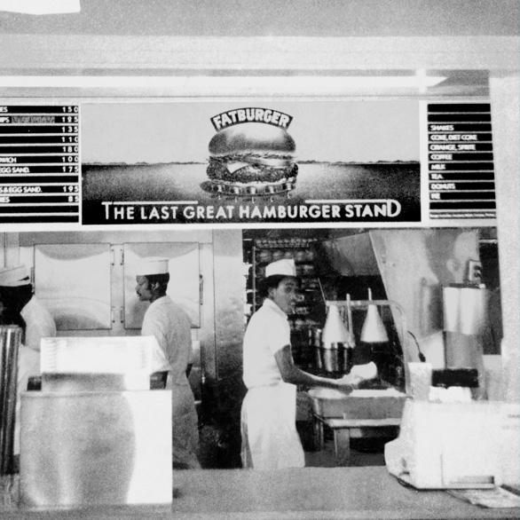 a black and white photo of fatburger workers behind the ordering desk