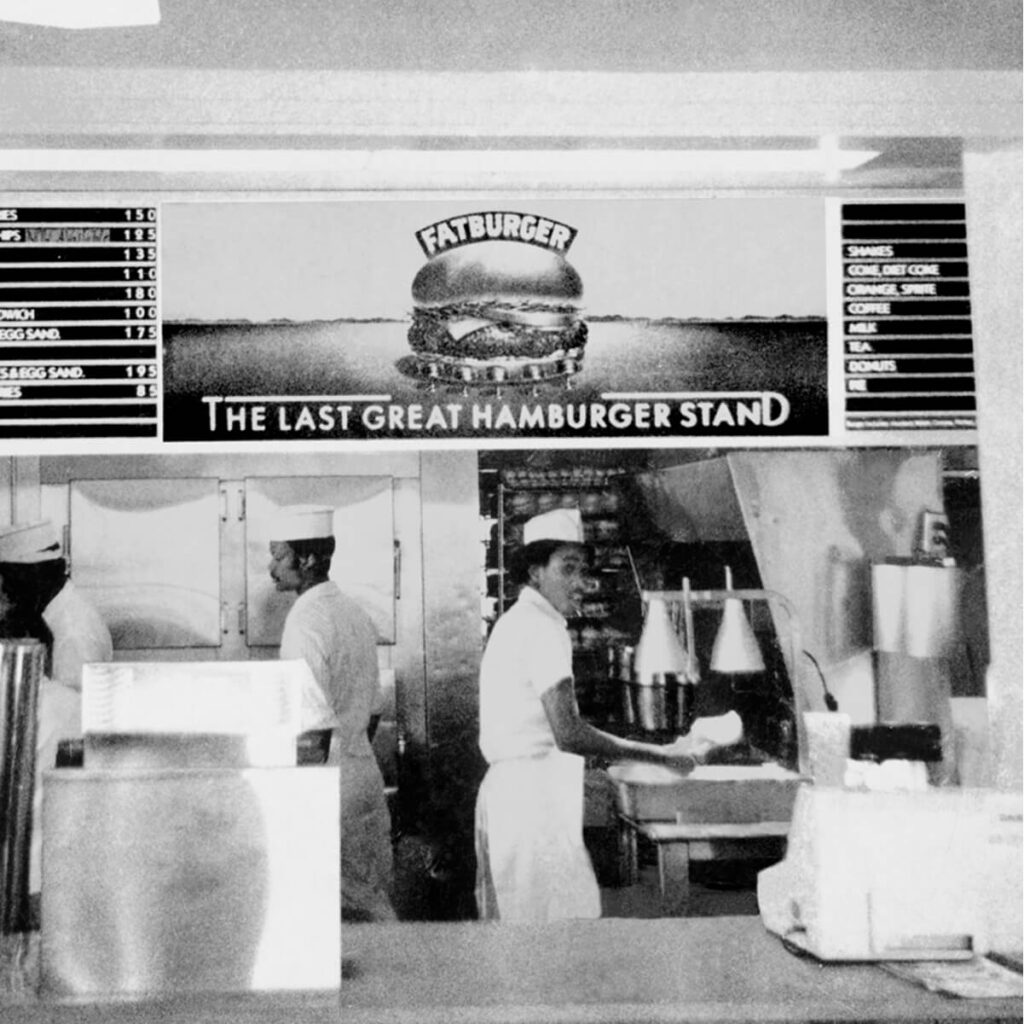 a black and white photo of fatburger workers behind the ordering desk